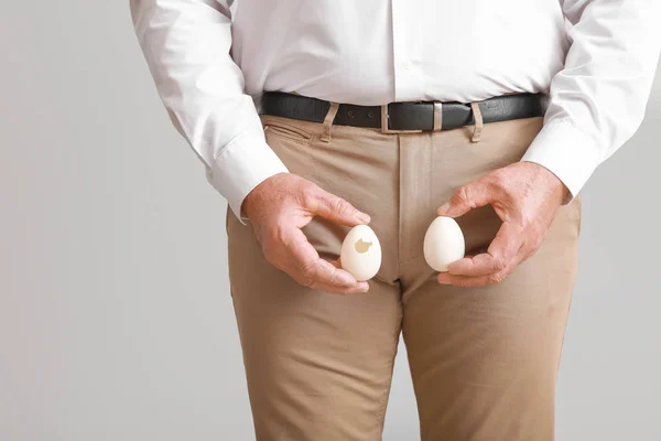 Mature man with eggs on light background. Urology concept — Stock Image Mature man with eggs on light background. Urology concept Royalty Free Stock Images