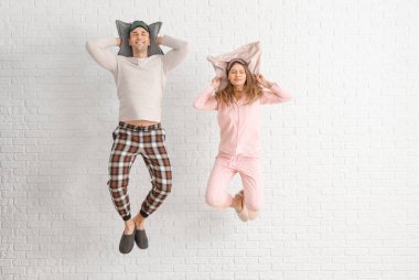 Pijamalı, beyaz tuğlalı arka planda yastıkları olan genç bir çift.