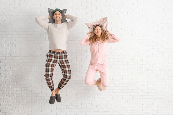 Jumping young couple in pajamas and with pillows on white brick background — Stock Photo, Image