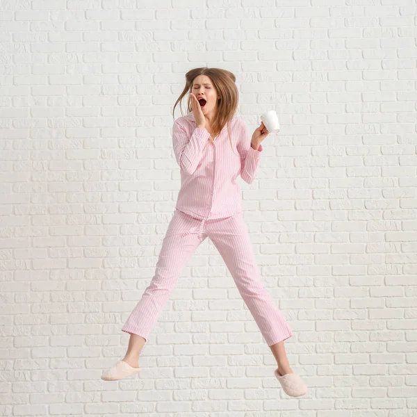 Ugrás álmos nő pizsamában és egy csésze kávé fehér tégla háttér — Stock Fotó