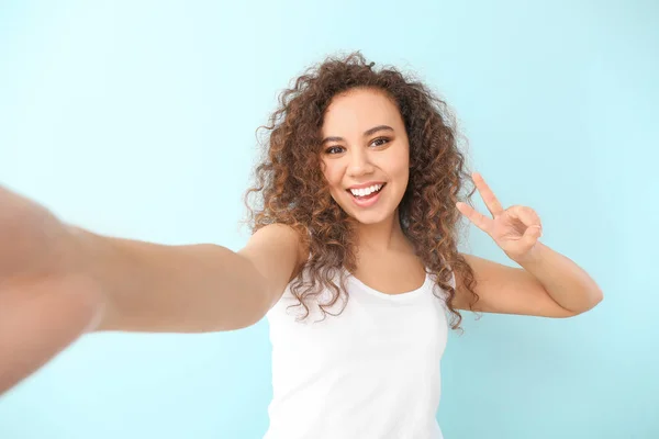 Mooie jonge vrouw het nemen van selfie op kleur achtergrond — Stockfoto