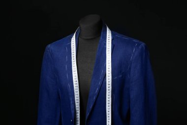 Yarısı bitmiş ceketi ve koyu arkaplanda şeridi olan manken.