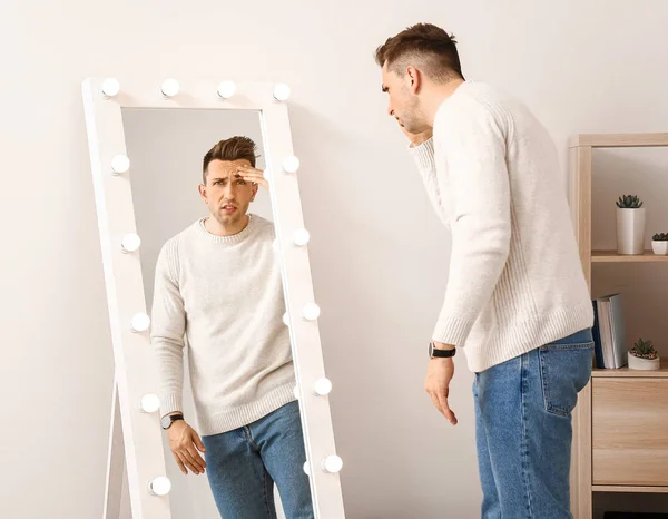 Displeased young man looking at his reflection in mirror — Stock Photo, Image