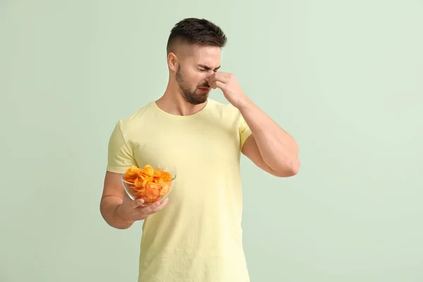 Displeased young man with potato chips on color background — Stock Photo, Image