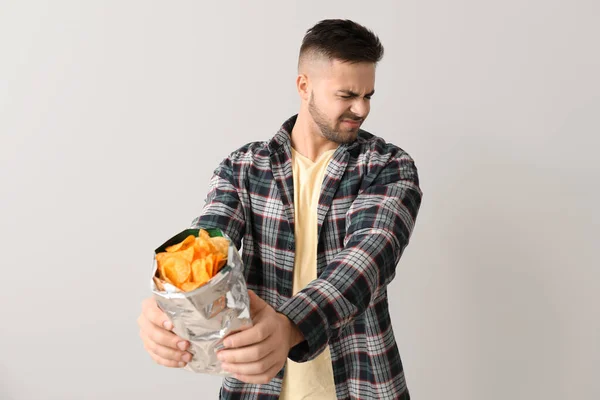 Displeased young man with potato chips on light background — Stock Photo, Image