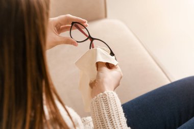 Young woman wiping eyeglasses at home, closeup