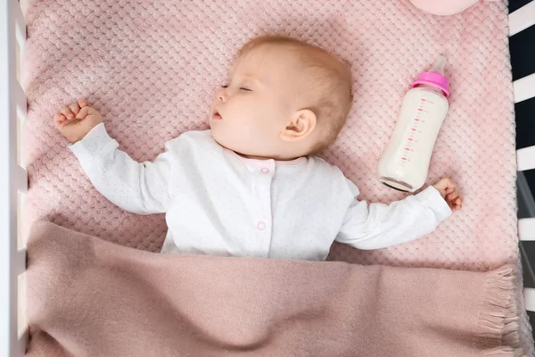 Sleeping baby with bottle of milk in crib — Stock Photo, Image