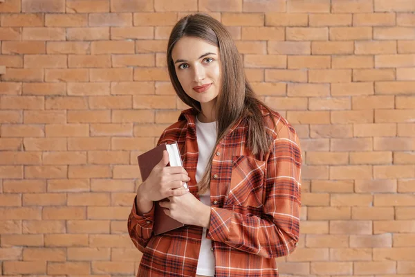 Hermosa joven con libro sobre fondo de ladrillo — Foto de Stock