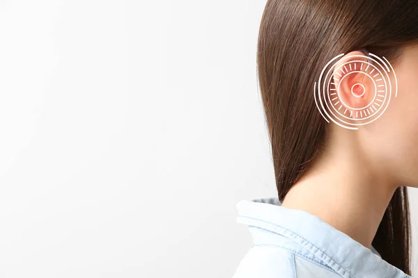 Young woman with hearing aid on light background — Stock Photo, Image