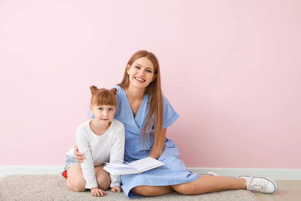 Beautiful young woman and her little daughter reading book near color wall — Stockfoto