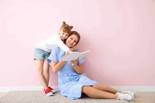 Frumoasă femeie tânără și fiica ei mai mică citind o carte lângă peretele color — Fotografie, imagine de stoc