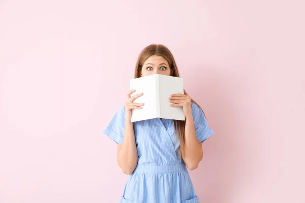 Shocked young woman with book on color background — Stock Photo, Image