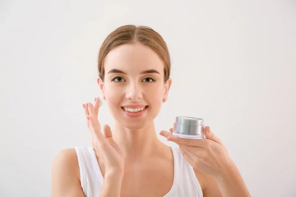 Hermosa joven con tarro de crema sobre fondo claro — Foto de Stock