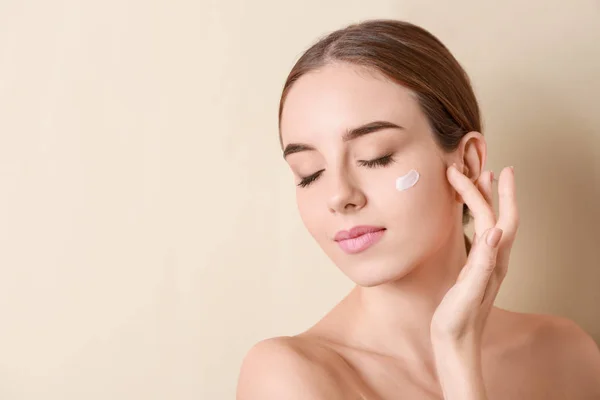 Hermosa mujer joven aplicando crema en su cara contra el fondo de color — Foto de Stock