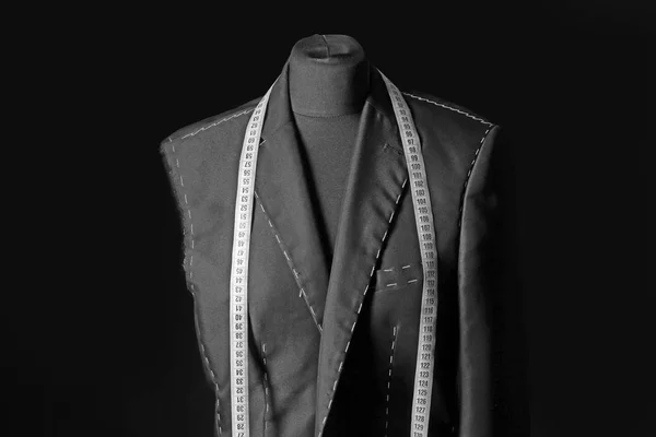 Tailor's mannequin with unfinished clothes and measuring tape on dark background — Stock Photo, Image