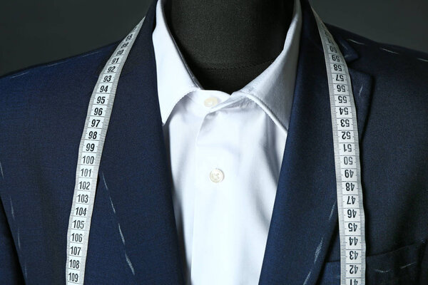 Tailor's mannequin with unfinished clothes and measuring tape on dark background, closeup