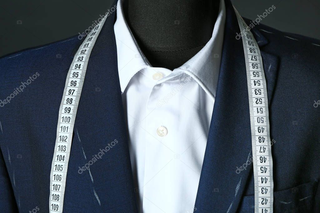 Tailor's mannequin with unfinished clothes and measuring tape on dark background, closeup