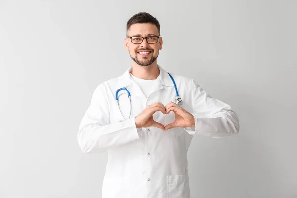 Muž kardiolog dělat srdce s rukama na světlém pozadí — Stock fotografie