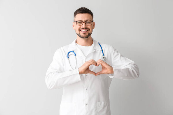 Male cardiologist making heart with his hands on light background