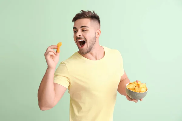 Handsome young man with tasty potato chips on color background — Stock Photo, Image