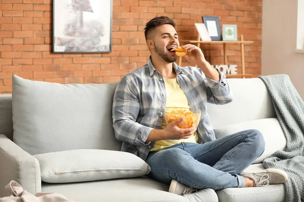 Handsome young man eating tasty potato chips at home — Stock Photo, Image