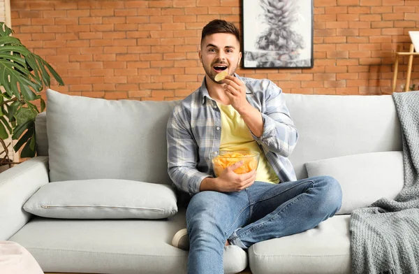 Handsome young man with tasty potato chips at home — Stock Photo, Image