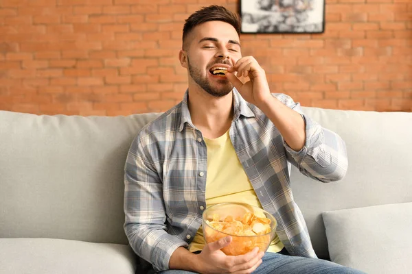 Guapo joven comiendo sabrosas papas fritas en casa — Foto de Stock