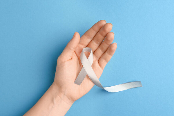 Female hand with silver ribbon on color background