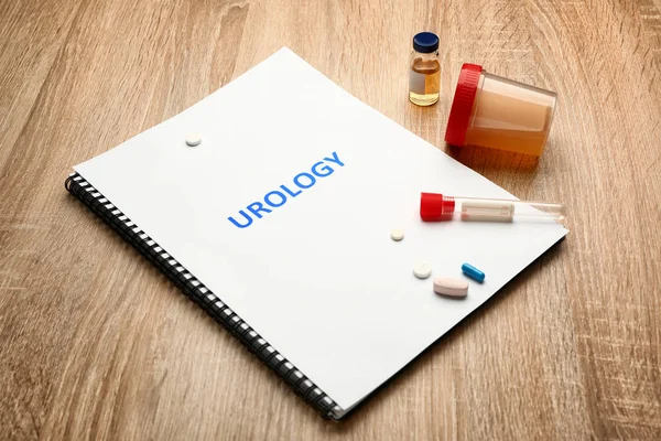 Caderno com texto UROLOGIA, medicamentos e amostras de urina sobre fundo de madeira — Fotografia de Stock
