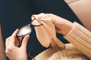 Young woman wiping eyeglasses at home, closeup