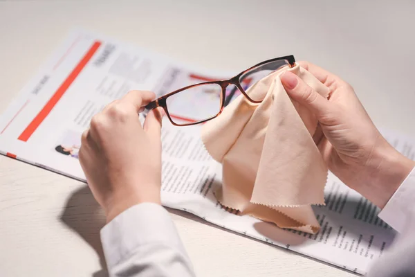 Young woman wiping eyeglasses at table, closeup — 스톡 사진