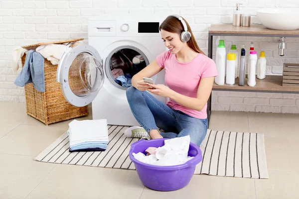 Young housewife listening to music while washing laundry at home — 스톡 사진