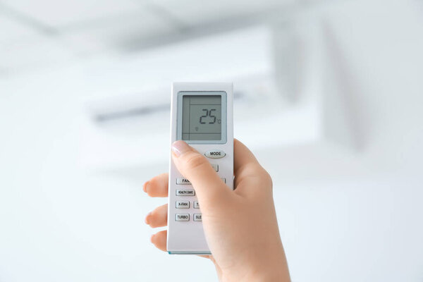 Young woman switching on air conditioner at home, closeup