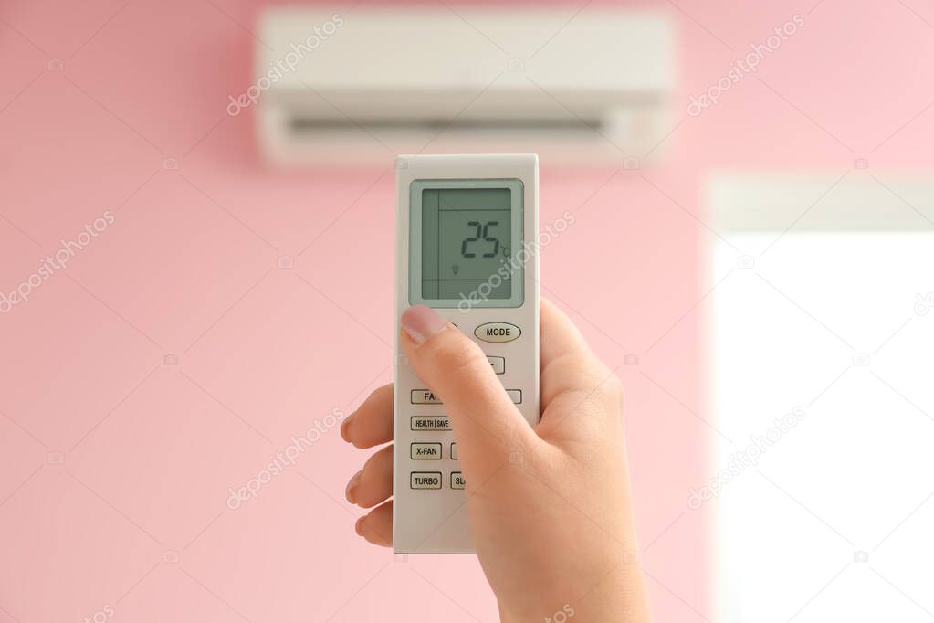 Young woman switching on air conditioner at home, closeup