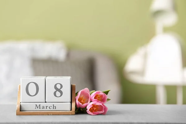 Calendar with date of International Women's Day and flowers on table in room — Stockfoto