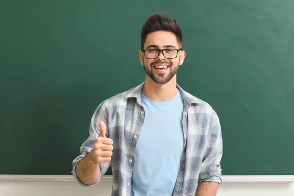 Männlicher Lehrer zeigt Daumen nach oben in der Nähe der Tafel im Klassenzimmer — Stockfoto