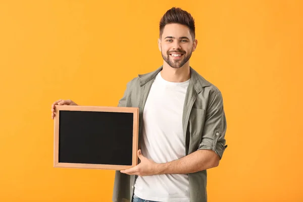 Young man with chalkboard on color background — 스톡 사진