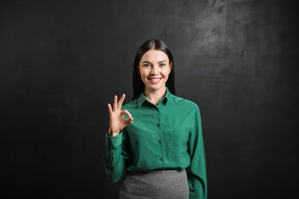 Kvinnlig lärare visar OK nära svarta tavlan i klassrummet — Stockfoto