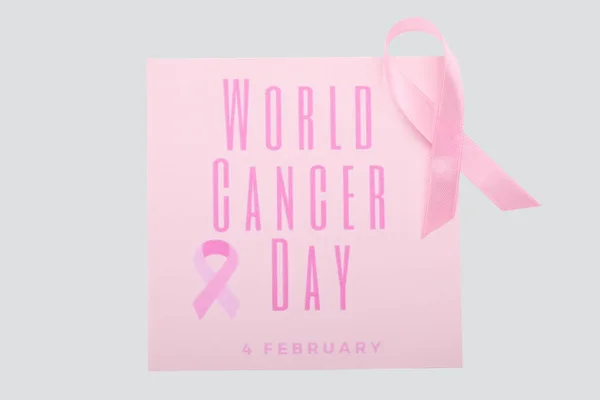 Pink ribbon and paper sheet with text WORLD CANCER DAY on white background