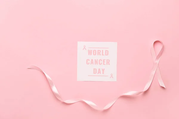 Pink ribbon and paper sheet with text WORLD CANCER DAY on color background