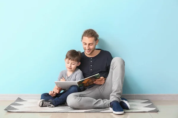 Vader en zijn zoontje lezen boek in de buurt van de lichtmuur — Stockfoto
