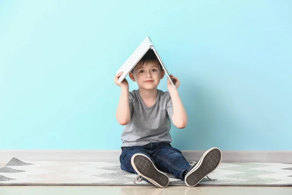 Netter kleiner Junge mit Buch in der Nähe der Lichtwand — Stockfoto