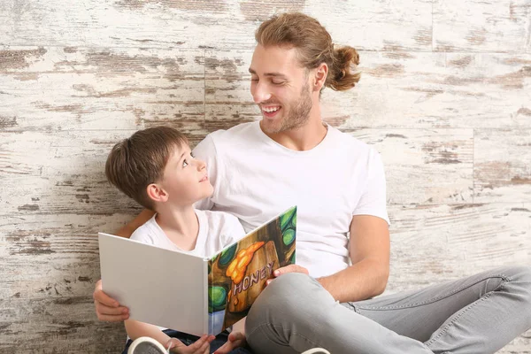 Padre y su pequeño hijo leyendo libro cerca de la pared de madera — Foto de Stock