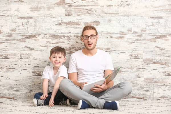 Padre y su pequeño hijo leyendo libro cerca de la pared de madera — Foto de Stock