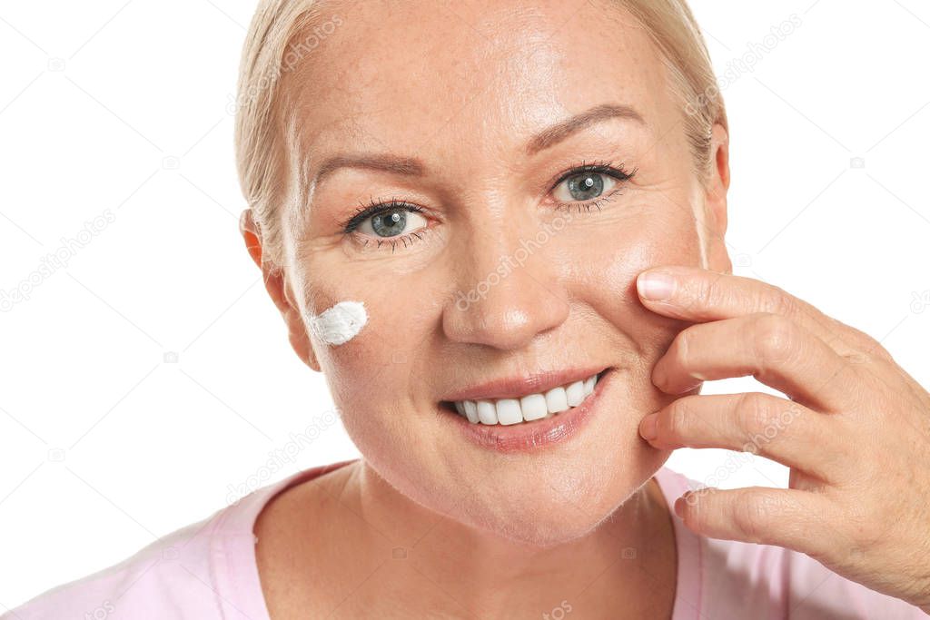 Beautiful mature woman applying facial cream against white background