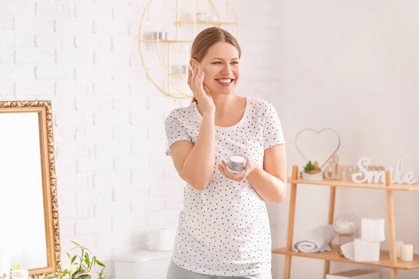 Красивая беременная женщина наносит крем в ванной комнате — стоковое фото