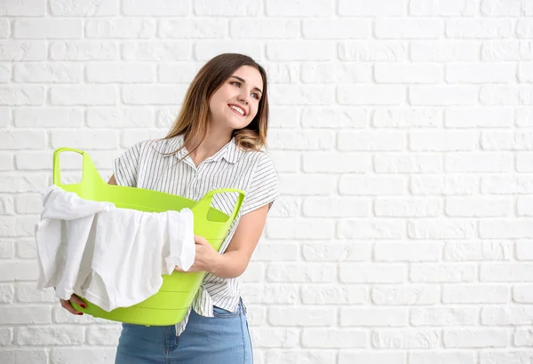 Beautiful young woman with laundry on white brick background — Stock Photo, Image