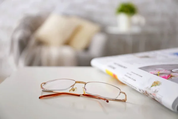 Stylish eyeglasses with newspaper on table at home — Stock Photo, Image