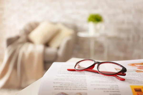 Stylish eyeglasses with newspaper on table at home — Stock Photo, Image