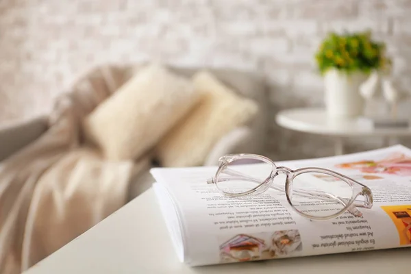 Stylish eyeglasses with newspaper on table at home — Stock Photo, Image